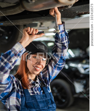 Female mechanic unscrew the nuts on the bottom of the car that is on the lift. A girl at a man's work. Female mechanic unscrew the nuts on the bottom of the car that is on the lift. A girl at a man's work. 101418573