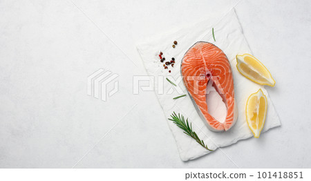 Raw salmon steak on a white board, lemon slices, spices. Top view on white table Raw salmon steak on a white board, lemon slices, spices. Top view on white table 101418851