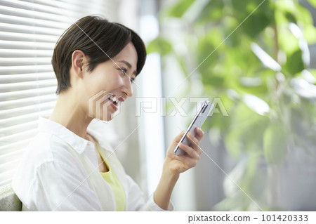 A middle-aged woman operating a smartphone by the window 101420333