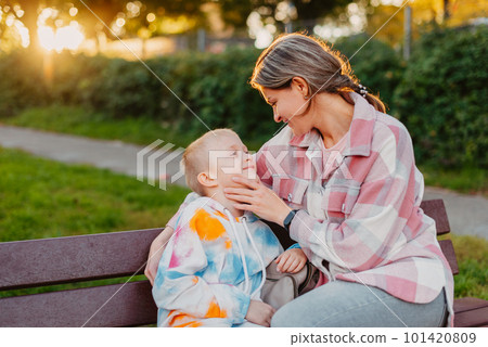 mother and son sit on a park bench in the rays of the setting sun. the concept of a family. Mother's Day. beautiful girl (mother) with a boy (son) in the park in the park are sitting on a bench at 101420809