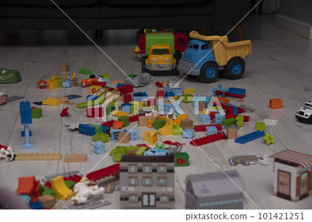 Children's toys are scattered on the floor in the living room.Parent steps on a children's constructor on the floor. 101421251