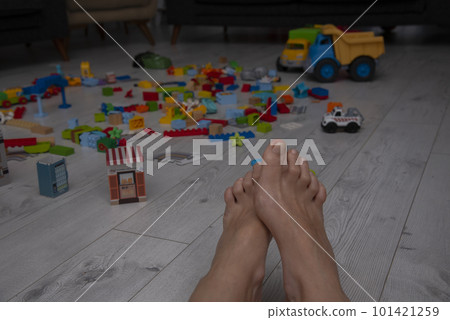 Children's toys are scattered on the floor in the living room.Parent steps on a children's constructor on the floor. Children's toys are scattered on the floor in the living room.Parent steps on a children's constructor on the floor. 101421259