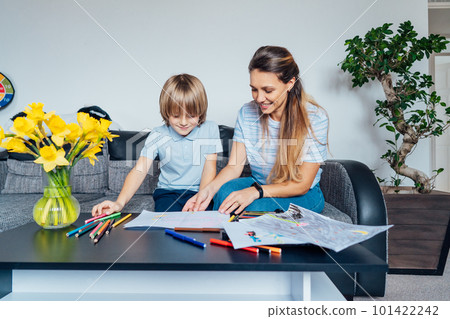 Mother and son drawing with color pencils and markers in the living room. Smiling mother has fun playing paint on paper with son on home family weekend, children creativity concept. Selective focus 101422242