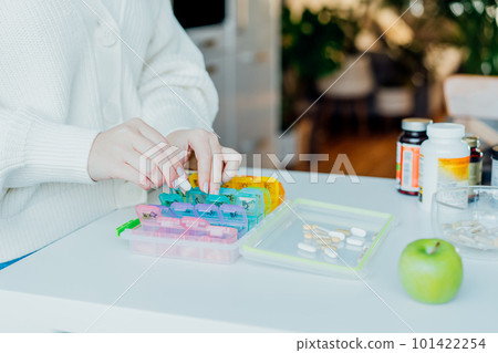 Woman's hands sorting pills into pills organizer. Close up medical pill box with daily doses of medicines. Antioxidant diet vitamin supplements for health and beauty care, biohacking concept 101422254