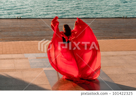 Sunrise red dress. A woman in a long red dress against the backdrop of sunrise, bright golden light of the sun's rays. The concept of femininity, harmony. 101422325