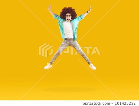 Happy funny boy in casual clothes and curly wig jumping and flying on yellow color background 101423252