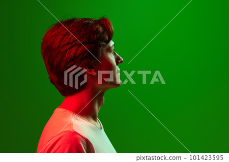 Profile view of handsome young man wearing white t-shirt over green neon background. Calmness, pacific Profile view of handsome young man wearing white t-shirt over green neon background. Calmness, pacific 101423595