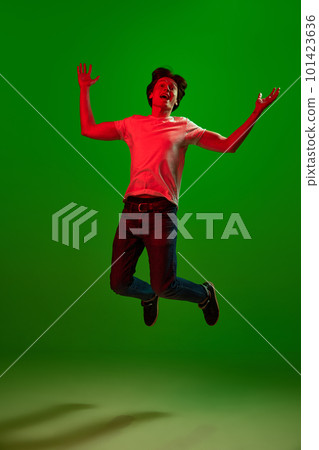 Studio shot of exciting guy, student screaming and jumping over green background in neon light. Encouraging news Studio shot of exciting guy, student screaming and jumping over green background in neon light. Encouraging news 101423636