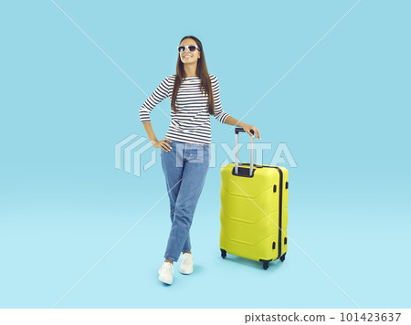 Happy woman in sunglasses standing with traveling suitcase on blue studio background 101423637