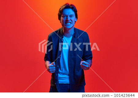 Studio shot of aggressive gay, man clenching his fists over red-orange background in neon light. Angry, furious Studio shot of aggressive gay, man clenching his fists over red-orange background in neon light. Angry, furious 101423644