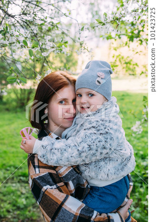 Young woman with her daughter in nature admires white flowering of spring trees Young woman with her daughter in nature admires white flowering of spring trees 101423725