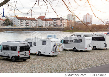 Many white modern campervan recreational motor home vehicles parked in row at camper park site Magdeburg city against Elbe river bridge. Motorhome campground stataion travel destination. RV lifestyle Many white modern campervan recreational motor home vehicles parked in row at camper park site Magdeburg city against Elbe river bridge. Motorhome campground stataion travel destination. RV lifestyle 101423884