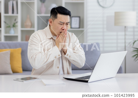 Shocked Asian man sitting at table at home and looking worriedly at laptop. Holds hands together, held bad news, financial problems, medical results. Shocked Asian man sitting at table at home and looking worriedly at laptop. Holds hands together, held bad news, financial problems, medical results. 101423995