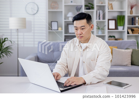 Serious and focused Asian man, businessman, freelancer, student working studying at home using laptop, Sitting at table and talking on video call, typing. Serious and focused Asian man, businessman, freelancer, student working studying at home using laptop, Sitting at table and talking on video call, typing. 101423996