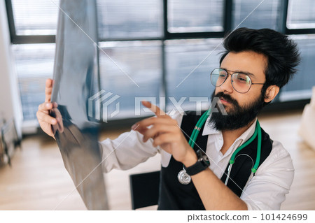 Close-up of pensive Indian male doctor in glasses thinking on diagnosis looking at MRI images scan, expressing concern of illness. Radiology physician examining spinal column x-ray image in hospital. Close-up of pensive Indian male doctor in glasses thinking on diagnosis looking at MRI images scan, expressing concern of illness. Radiology physician examining spinal column x-ray image in hospital. 101424699