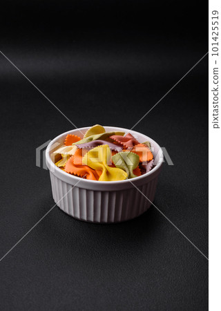 Raw farfalle pasta in different colors on a dark concrete background Raw farfalle pasta in different colors on a dark concrete background 101425519