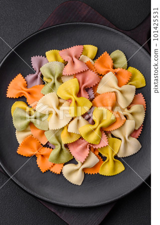 Raw farfalle pasta in different colors on a dark concrete background 101425531