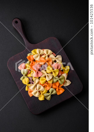 Raw farfalle pasta in different colors on a dark concrete background 101425536