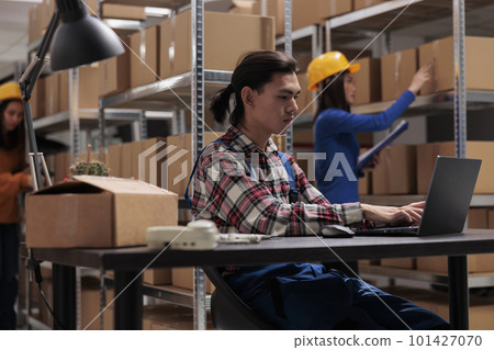 Young asian warehouse supervisor using laptop in storage room. Storehouse worker supervising inventory management in computer software and checking goods quality control system Young asian warehouse supervisor using laptop in storage room. Storehouse worker supervising inventory management in computer software and checking goods quality control system 101427070