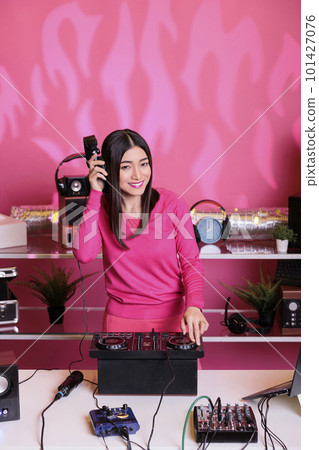 Smiling musician standing at dj table playing electronic music using professional turntables, having fun in studio over pink background. Artist doing performance at nightclub with audio equipment Smiling musician standing at dj table playing electronic music using professional turntables, having fun in studio over pink background. Artist doing performance at nightclub with audio equipment 101427076