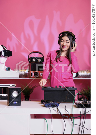 Artist wearing headset while mixing electronic sound with techno at professional mixer console, having fun at night in club. Asian musician standing at dj table performing music, celebrating album Artist wearing headset while mixing electronic sound with techno at professional mixer console, having fun at night in club. Asian musician standing at dj table performing music, celebrating album 101427077