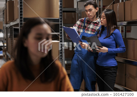 Retail storehouse workers picking customer order using checklist on clipboard. Industrial warehouse employees standing near parcels shelf, analyzing goods list and doing inventory 101427100
