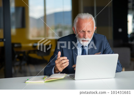 Handsome smiling senior man while sitting at his cozy workplace with laptop at home, retired male chatting with friends in social media, 101431681