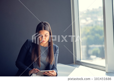 Young attractive female manager working on digital tablet while standing in modern office Young attractive female manager working on digital tablet while standing in modern office 101431686