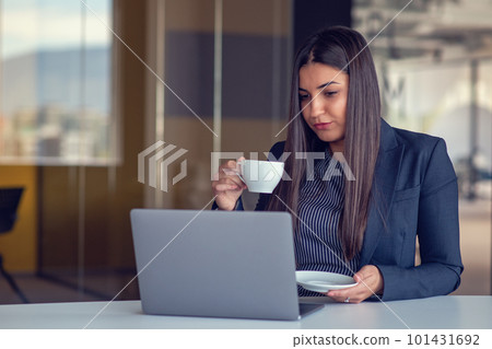Young woman working on laptop and drinking coffee in office Young woman working on laptop and drinking coffee in office 101431692
