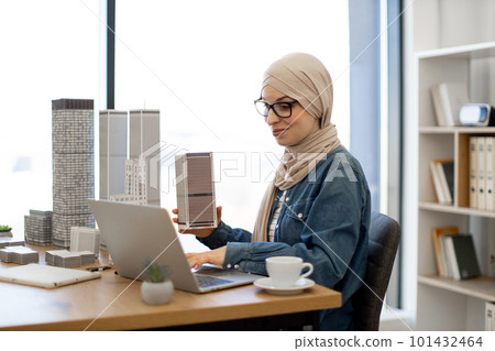 Female holding model while typing on computer indoors Female holding model while typing on computer indoors 101432464