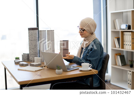 Woman at writing desk holding building model in office 101432467