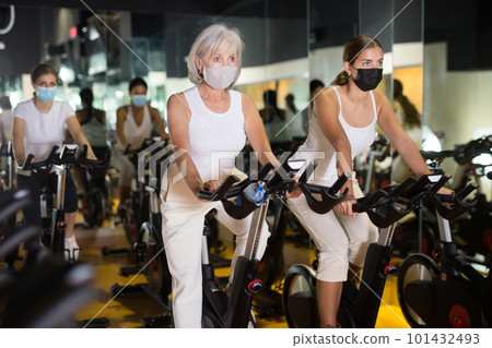 Women in masks training on stationary bikes Women in masks training on stationary bikes 101432493