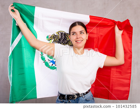 Joyous young woman holding Mexico flag against unicoloured background Joyous young woman holding Mexico flag against unicoloured background 101432585