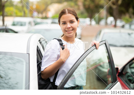 Portrait of a positive girl standing near an open car 101432612