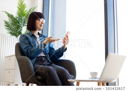 Woman sitting in office and using smartphone for video chat Woman sitting in office and using smartphone for video chat 101432617