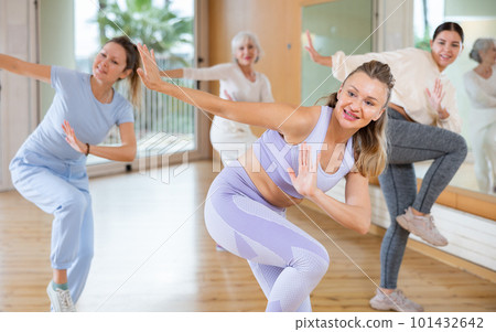 Class of happy women of different ages in sportswear training with knee up while learning dance moves with trainer in gym Class of happy women of different ages in sportswear training with knee up while learning dance moves with trainer in gym 101432642