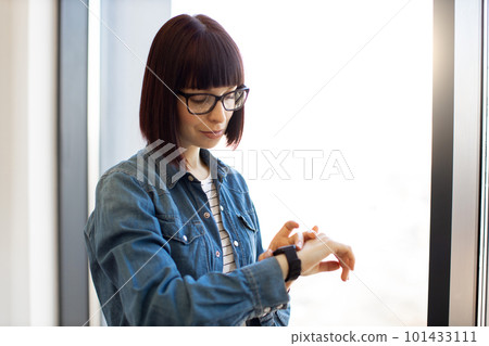 Woman touching screen of smartwatch on wrist at office 101433111