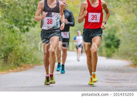 group male runners athletes running race in park road, autumn marathon, fallen yellow leaves on ground 101433203