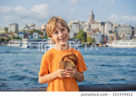 Boy in Istanbul having breakfast with Simit and a glass of Turkish tea. Glass of Turkish tea and bagel Simit against golden horn bay and the Galata Tower in Istanbul, Turkey. Turkiye. Traveling with 101434952
