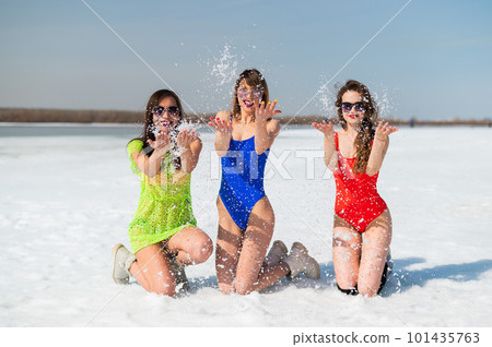 Three girlfriends in swimsuits are relaxing on a snow-covered beach. Hot girls posing in bikinis outdoors in winter. Three girlfriends in swimsuits are relaxing on a snow-covered beach. Hot girls posing in bikinis outdoors in winter. 101435763