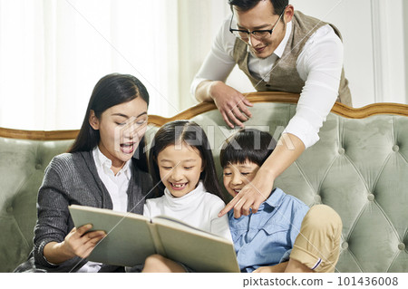 young asian parents and two children sitting on couch reading book together in family living room at home young asian parents and two children sitting on couch reading book together in family living room at home 101436008