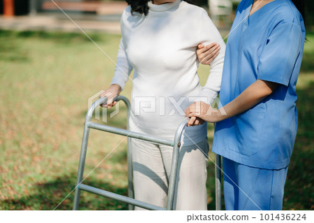 Asian careful caregiver or nurse and the happy patient in a wheelchair are walking in the garden to help and encourage and rest your mind with green nature. Help support yourself to learn to walk. 101436224