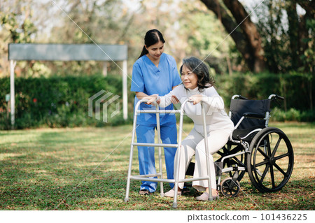 Asian careful caregiver or nurse and the happy patient in a wheelchair are walking in the garden to help and encourage and rest your mind with green nature. Help support yourself to learn to walk. Asian careful caregiver or nurse and the happy patient in a wheelchair are walking in the garden to help and encourage and rest your mind with green nature. Help support yourself to learn to walk. 101436225