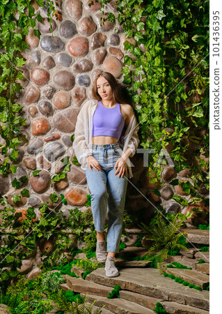 Cute woman leaning on old stone wall overgrown with plants 101436395