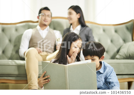 two asian children sitting on floor in family living room reading book together 101436550