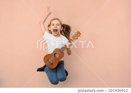 Emotional little jumping girl playing guitar like rock star on pink background Emotional little jumping girl playing guitar like rock star on pink background 101436912
