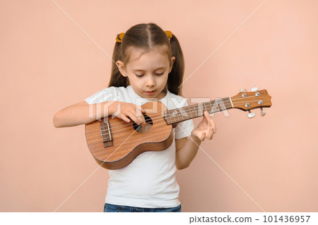 Preschool girl learning music by playing ukulele 101436957