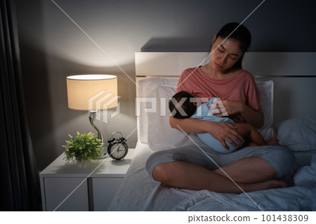 sleepy and tired mother breastfeeding newborm baby on bed at night sleepy and tired mother breastfeeding newborm baby on bed at night 101438309