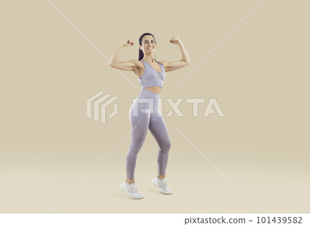 Beautiful sporty woman showing off athletic body and muscular arms on beige background. 101439582