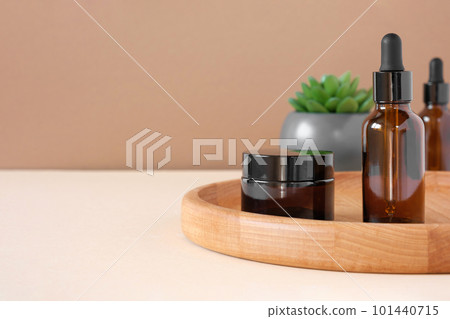 Glass bottles on wooden plate. Natural skin care SPA beauty product design. Mineral organic oil cosmetics on beige background. Earth tones. Mock-Up. Oily pipette. Face and body treatment. Front View Glass bottles on wooden plate. Natural skin care SPA beauty product design. Mineral organic oil cosmetics on beige background. Earth tones. Mock-Up. Oily pipette. Face and body treatment. Front View 101440715